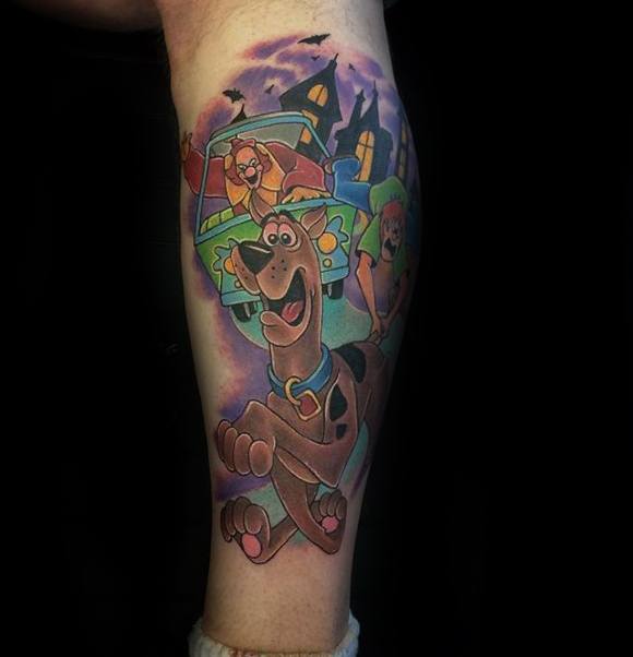 Colorful tattoo of Scooby-Doo running joyfully in front of the Mystery Machine, with Shaggy and a haunted house in the spooky background.