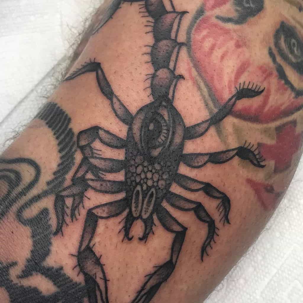 Tattoo of a black scorpion with a third eye on its back, inked in bold shading and fine details on the arm.