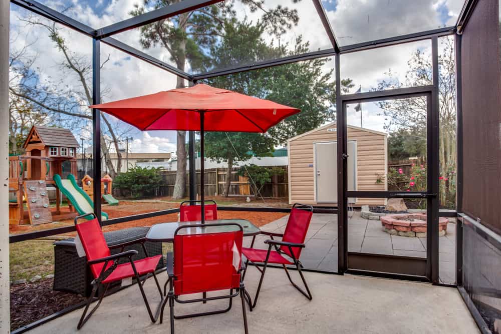 enclosed glass window wall patio red outdoor furniture glass table red umbrella playground