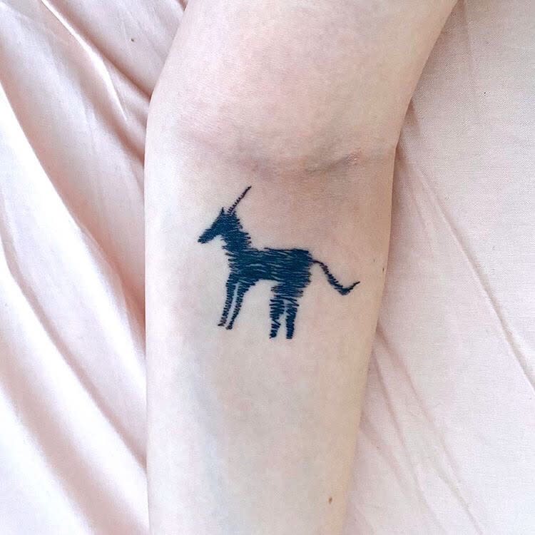 Minimalist black ink unicorn tattoo with a rough, hand-drawn texture, creating a simple yet artistic silhouette on the forearm.