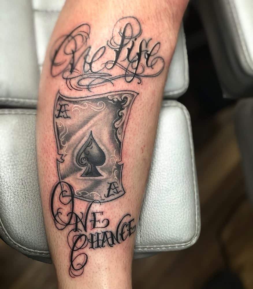 A black-and-white tattoo featuring the Ace of Spades card with intricate details, with the phrase "One Life One Chance" 