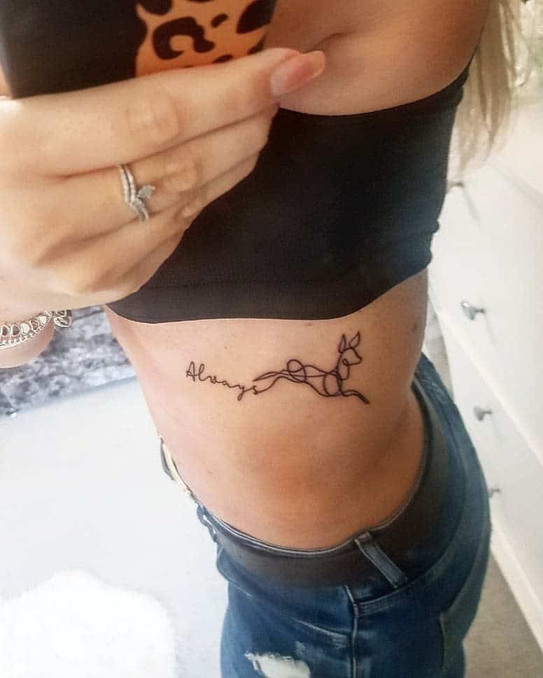 Elegant rib tattoo with 'Always' in cursive connected to a flowing deer outline, symbolizing eternal loyalty and grace