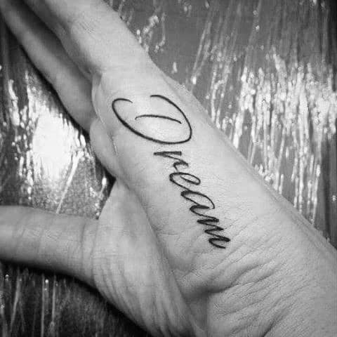 Side of the hand tattoo with the word “Dream” in elegant cursive script, placed along the edge of the palm.