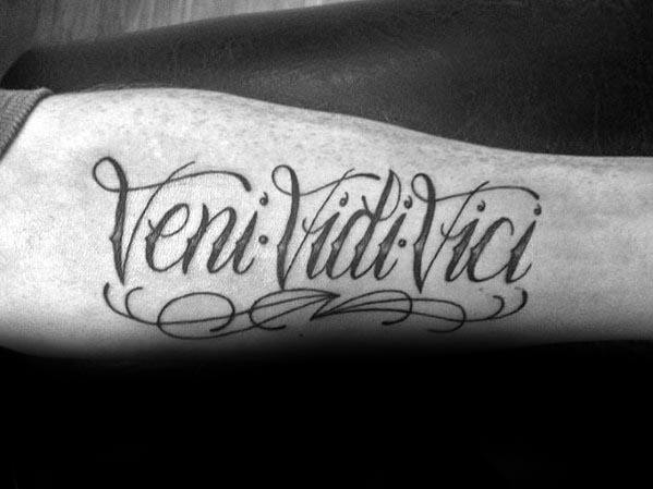 Tattoo on an arm reading "Veni Vidi Vici" in cursive script