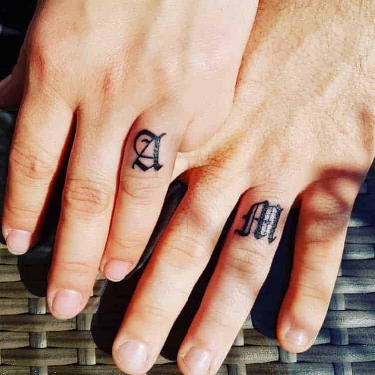 Two hands with "A" and "M" tattoos on ring fingers