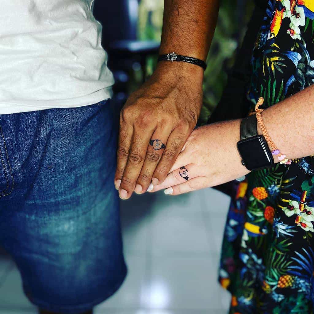 Matching wedding ring tattoos featuring a letter 'R' and 'P' or design, signifying a deep bond