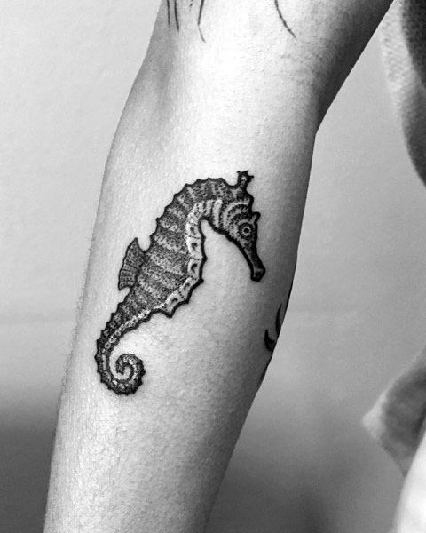 Small black and grey seahorse tattoo on forearm, featuring fine linework and subtle shading for a delicate and detailed marine-inspired design.