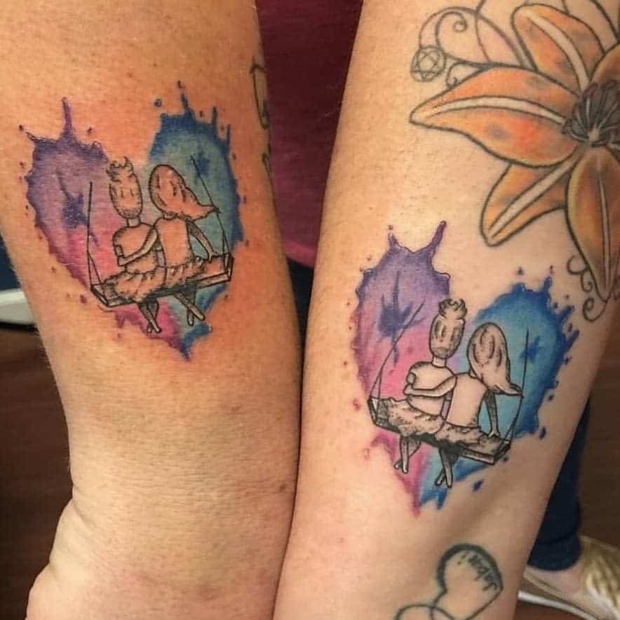Tattoos of two sisters sitting on a swing within watercolor heart shapes, with blue and purple hues