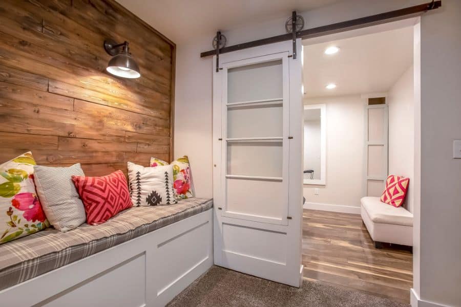 Cozy banquette seating area with colorful pillows, wood accent wall, and white sliding barn door.