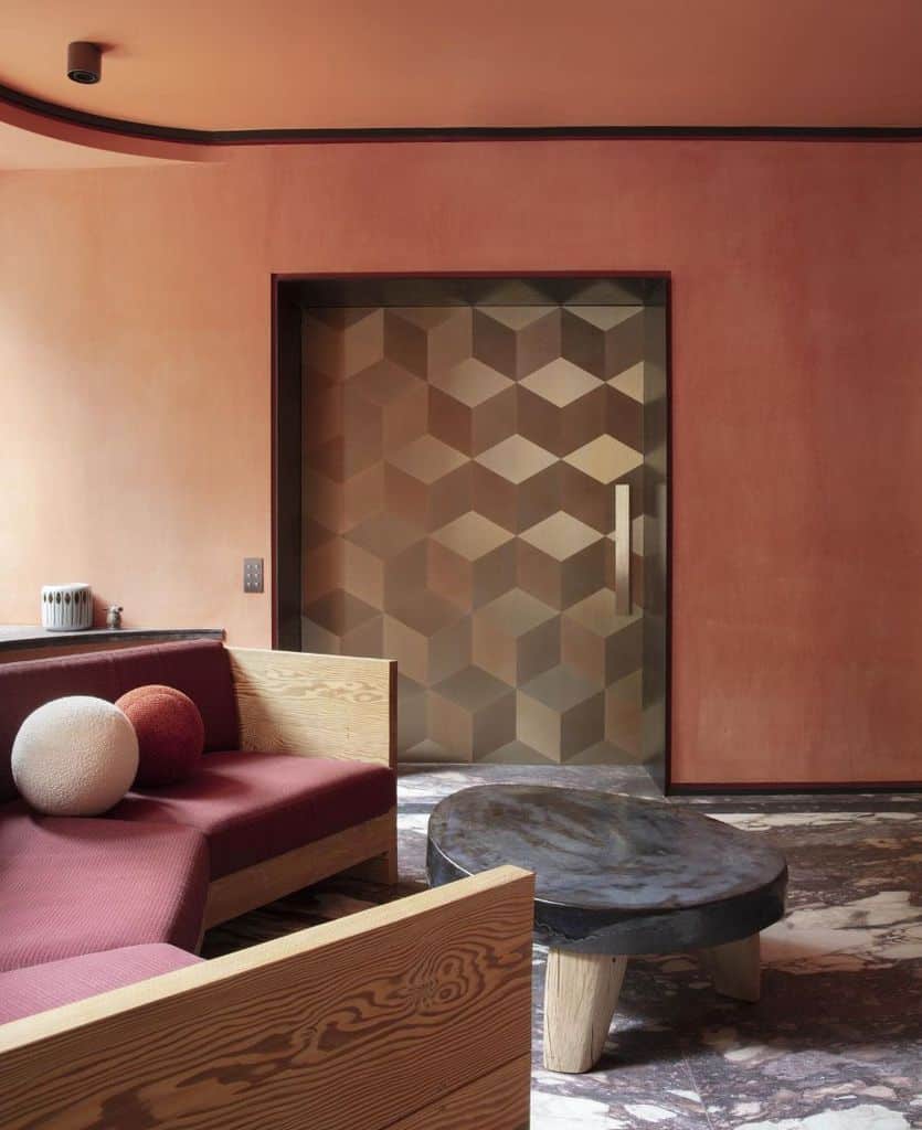 Abstract living room with angular wooden couch, round table, and geometric-patterned door.