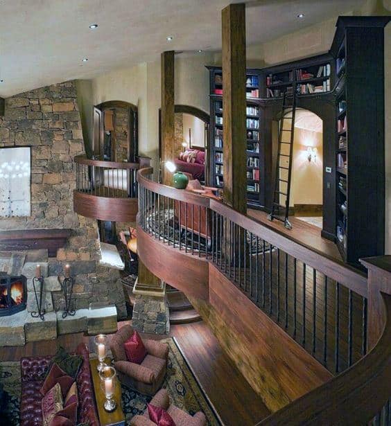 Cozy library with a curved wooden balcony overlooking a stone fireplace and comfortable seating area
