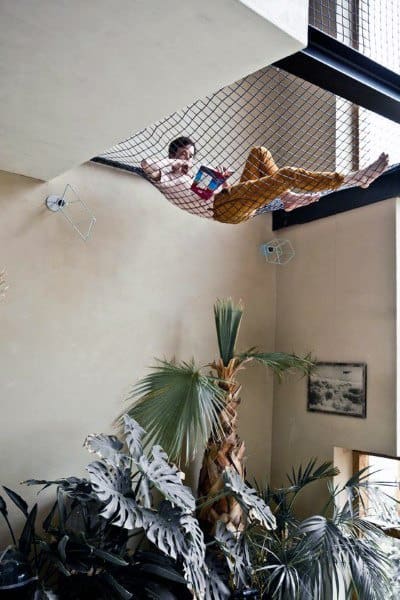 Suspended net hammock above a lush indoor garden in a modern, light-filled space.