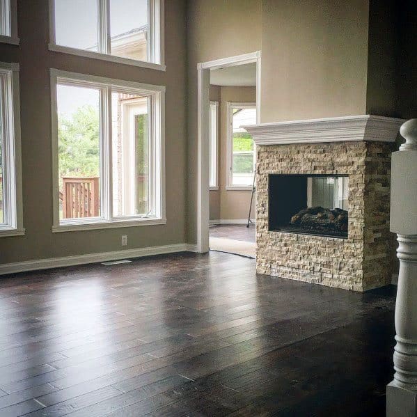Modern living room with large windows, hardwood floor, and a stacked stone fireplace