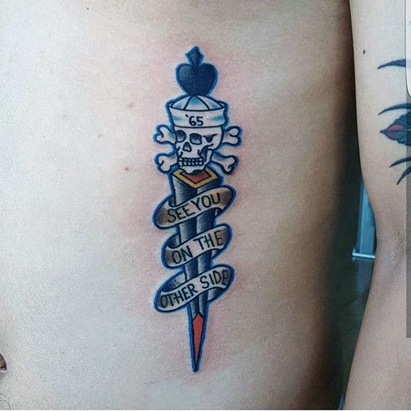 Tattoo of a skull wearing a '65 hat, cross bones beneath it, and a dagger with a ribbon saying "See You On The Other Side"