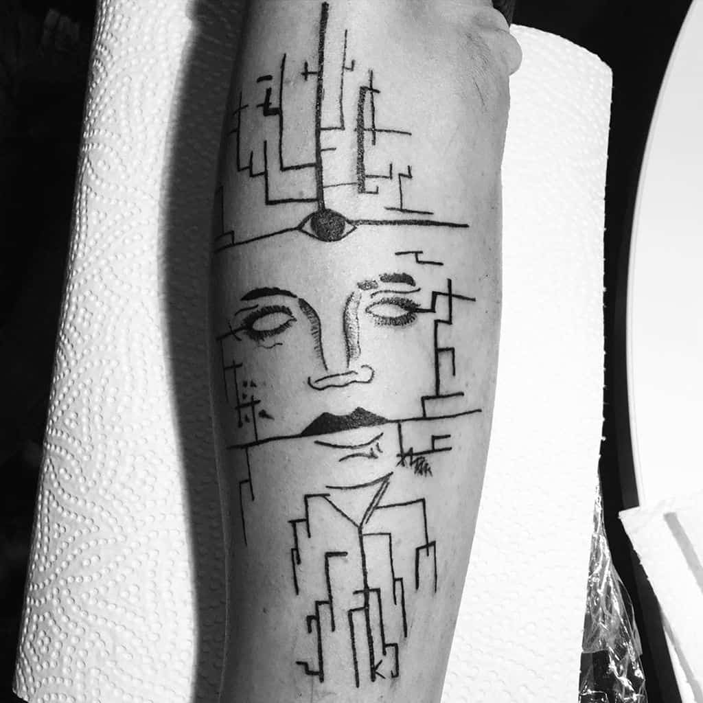 Tattoo of a fragmented abstract face with a third eye, combined with geometric cityscape elements, inked in fine black lines on the forearm.