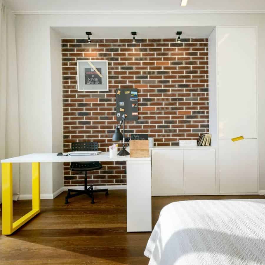 Bedroom office with white desk, exposed brick wall, and modern lighting.
