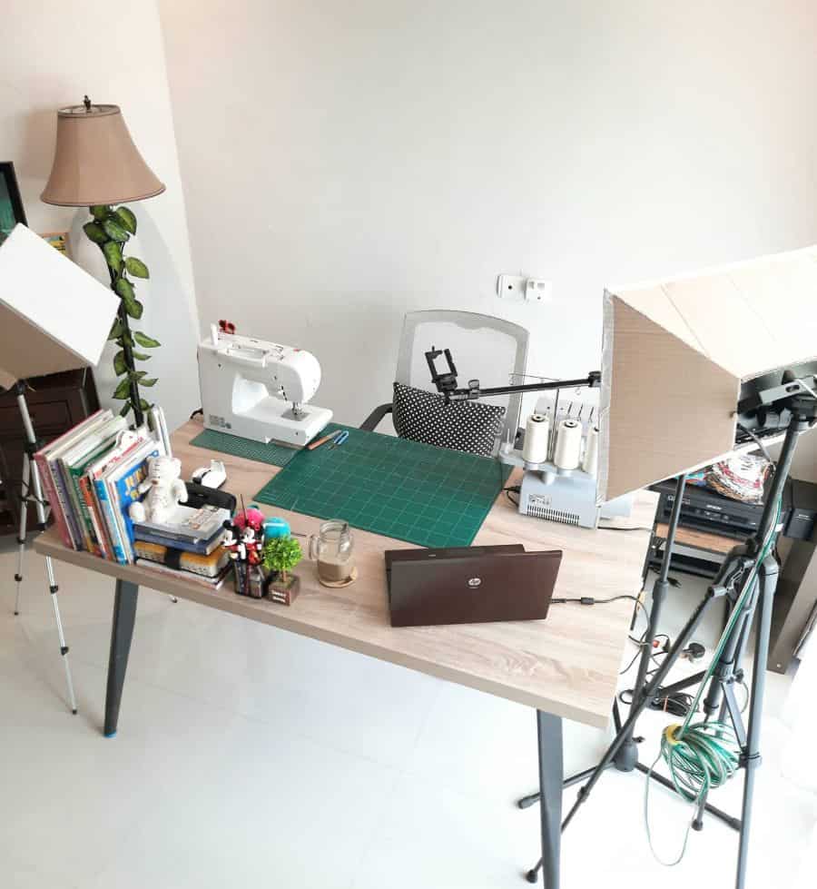 Multifunctional sewing desk with sewing machines, cutting mat, books, and video setup for creative projects