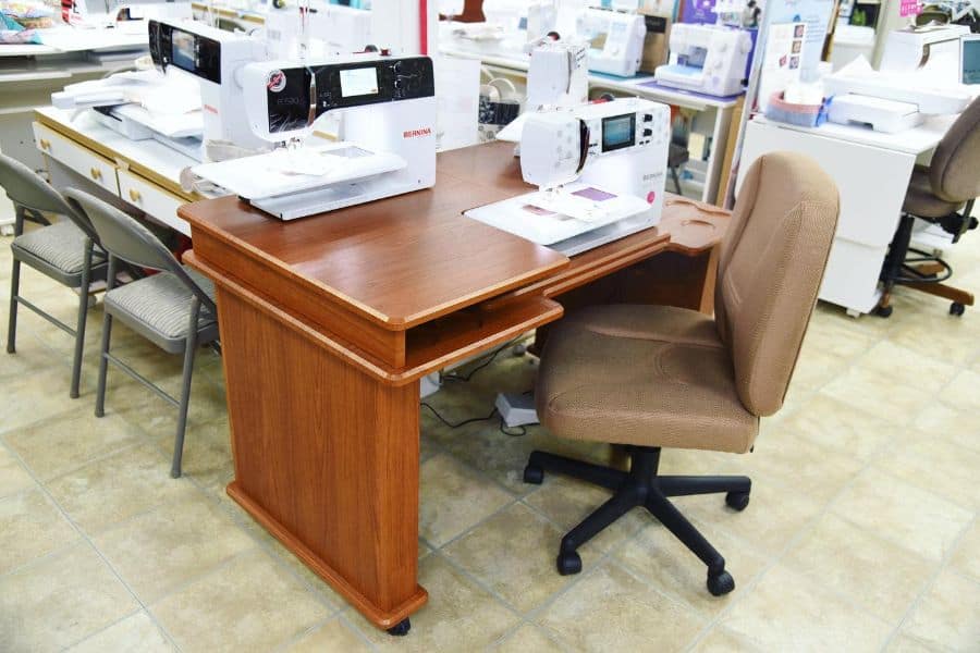 Spacious sewing table with a wooden finish, equipped with modern sewing machines and a comfortable upholstered chair, ideal for crafting sessions