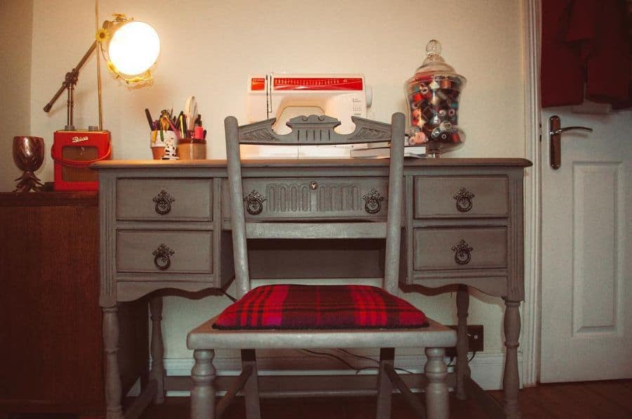 Vintage-style sewing station with a classic wooden desk, red plaid cushion, and cozy lighting for creative projects.