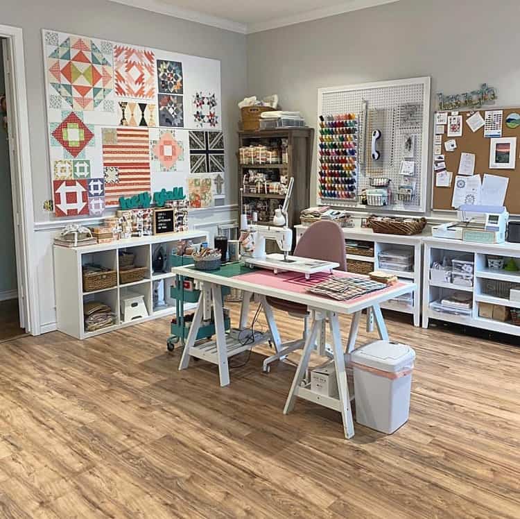 Bright craft room with a sewing station, colorful quilt wall, organized shelves, and corkboard on the wall