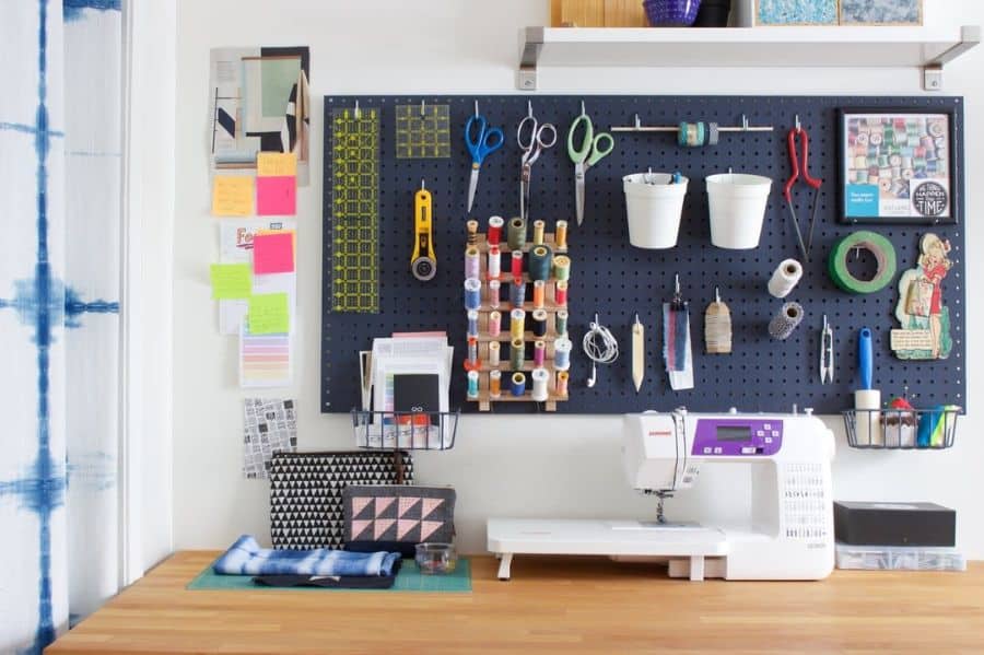 Craft room with sewing machine, pegboard with tools, thread, and fabric on a wooden table