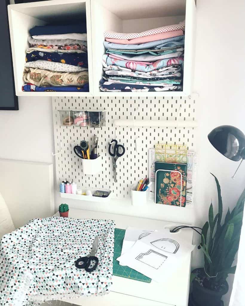 Compact sewing workspace with fabric storage, a pegboard for tools, cutting materials, and a stylish desk lamp