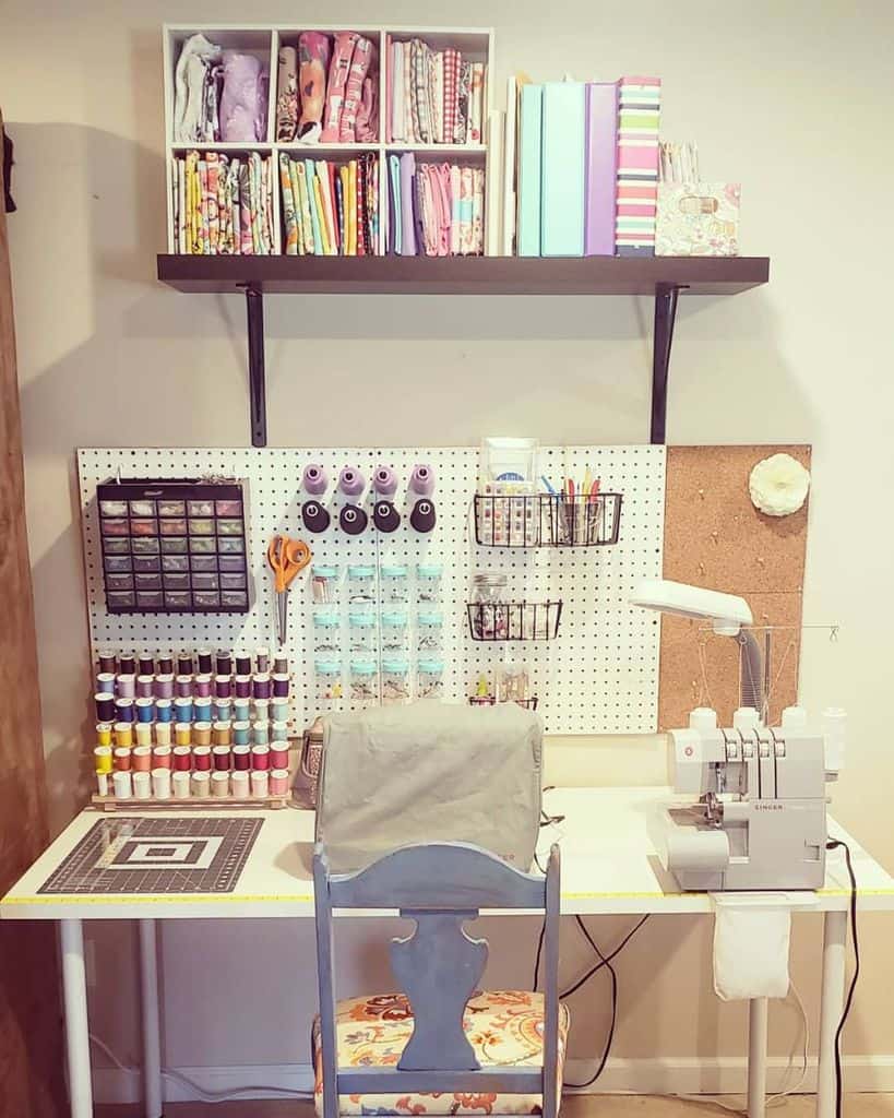 Sewing workspace with fabric, thread, and supplies organized on pegboard, shelves and a table