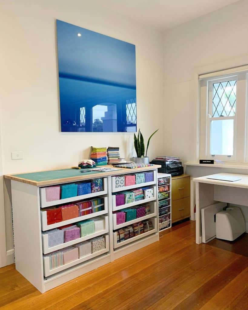 Bright sewing room with organized fabric storage featuring clear drawers for easy color and pattern selection, set against a polished hardwood floor and modern decor