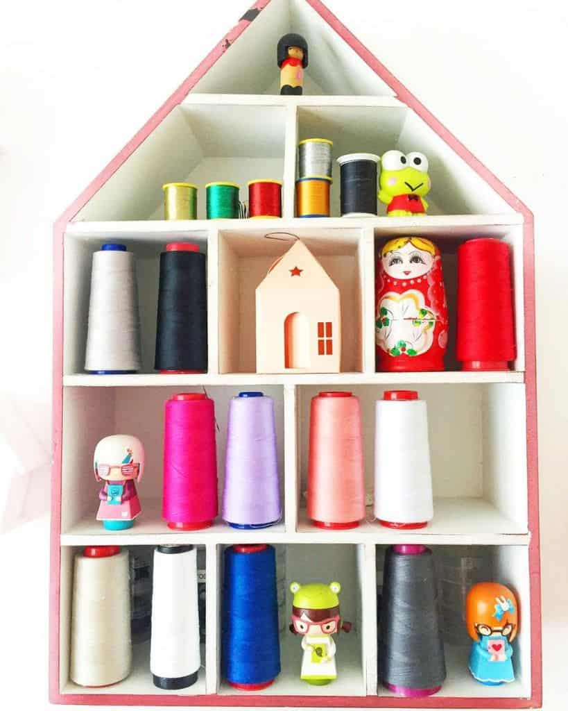 Creative thread storage in a house-shaped shelf with colorful threads and charming decorative figurines, adding a playful touch to the sewing room