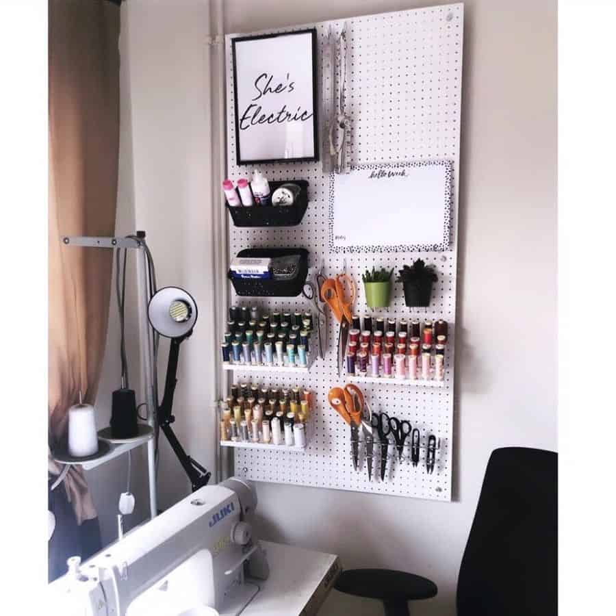 Wall-mounted pegboard featuring organized storage for thread spools, scissors, and crafting supplies, complete with motivational artwork and a mini whiteboard for notes