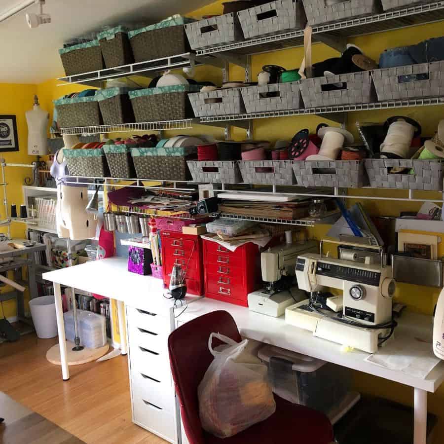 Bright sewing room with wall-mounted shelves holding neatly arranged storage baskets, vintage sewing machines, and vibrant red drawers for additional organization