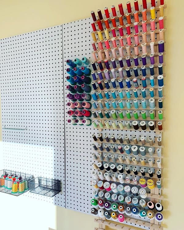 A wall-mounted pegboard with colorful thread spools organized by shade and metal baskets at the bottom