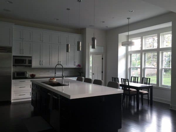 Modern kitchen with a large island, sleek cabinets, pendant lights, and dining table by a window overlooking the yard