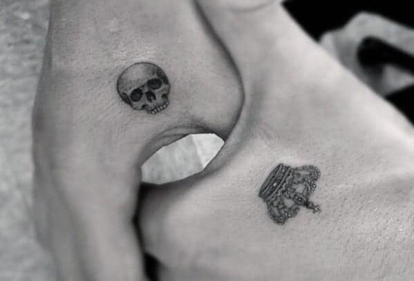 Close-up of a tiny skull tattoo and a small crown tattoo on the inside of two thumbs
