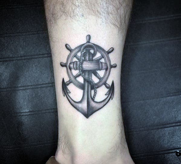 Black and gray anchor and ship wheel tattoo on the ankle, featuring intricate shading and fine details, symbolizing stability, direction, and nautical heritage.