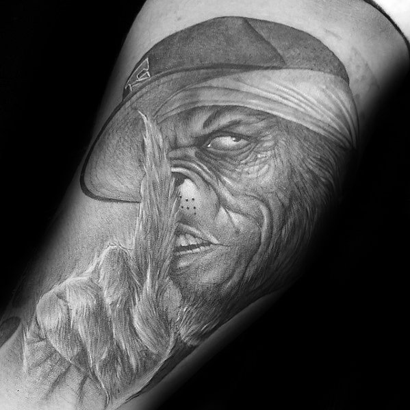 Grinch character wearing a cap, with a finger on his lips in a "shh" gesture, depicted in detailed black and grey shading for a bold and dramatic tattoo design.