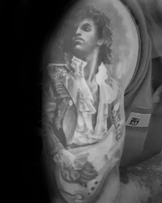 Black and white tattoo of Prince with a guitar on a person's arm