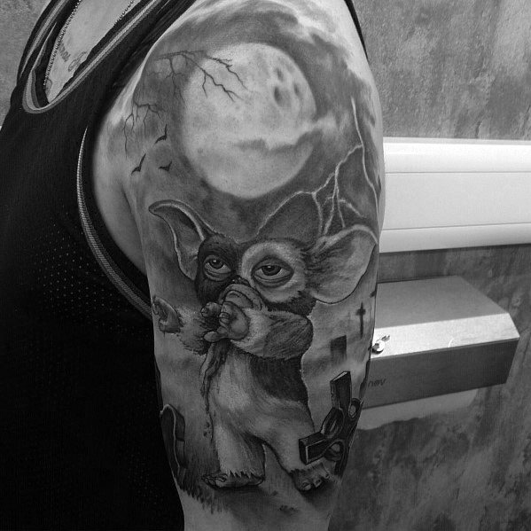Black and gray Gizmo tattoo with a spooky graveyard scene, full moon, and eerie details, blending innocence with a dark atmosphere.