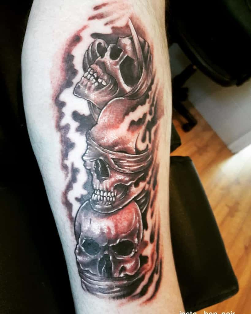 Dark, shaded tattoo of three stacked skulls with blindfolds and gags, symbolizing 'Hear No Evil, See No Evil, Speak No Evil,' surrounded by a smoky aura