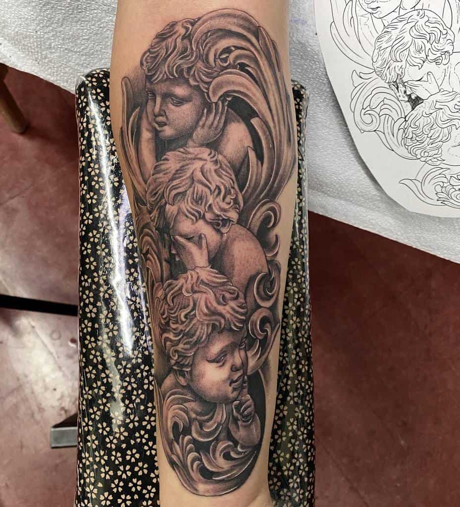 Intricate forearm tattoo of three cherubic figures in 'Hear No Evil, See No Evil, Speak No Evil' poses, surrounded by ornate swirls