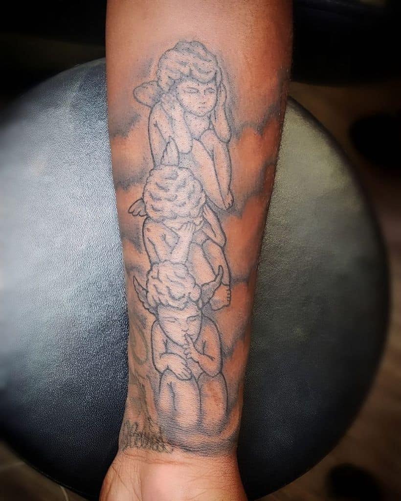 Tattoo of three cherubs on an arm, each covering eyes, ears, and mouth, symbolizing "see no evil, hear no evil, speak no evil"
