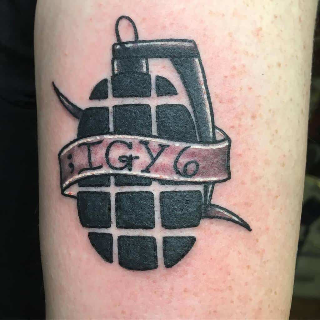 Tattoo of a grenade with a ribbon wrapped around it displaying the text ";TGY6" on skin