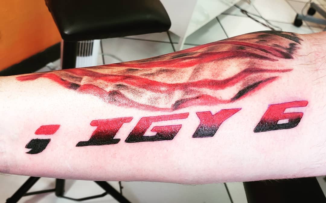 Forearm tattoo of ';IGY6' in bold red and black lettering, with a shaded American flag design in the background