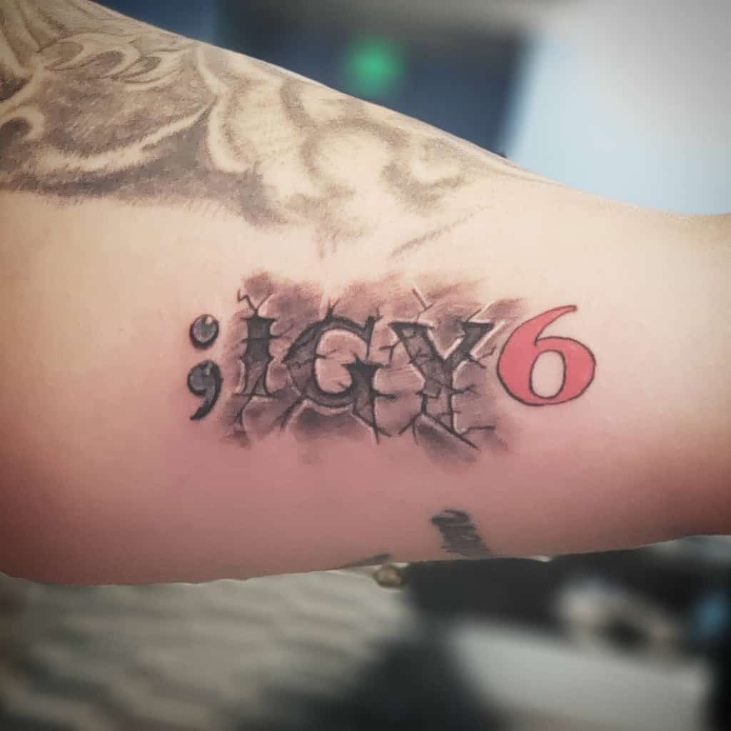 Tattoo on an arm with a semicolon followed by "IGY6" in cracked letters, with the number 6 in red