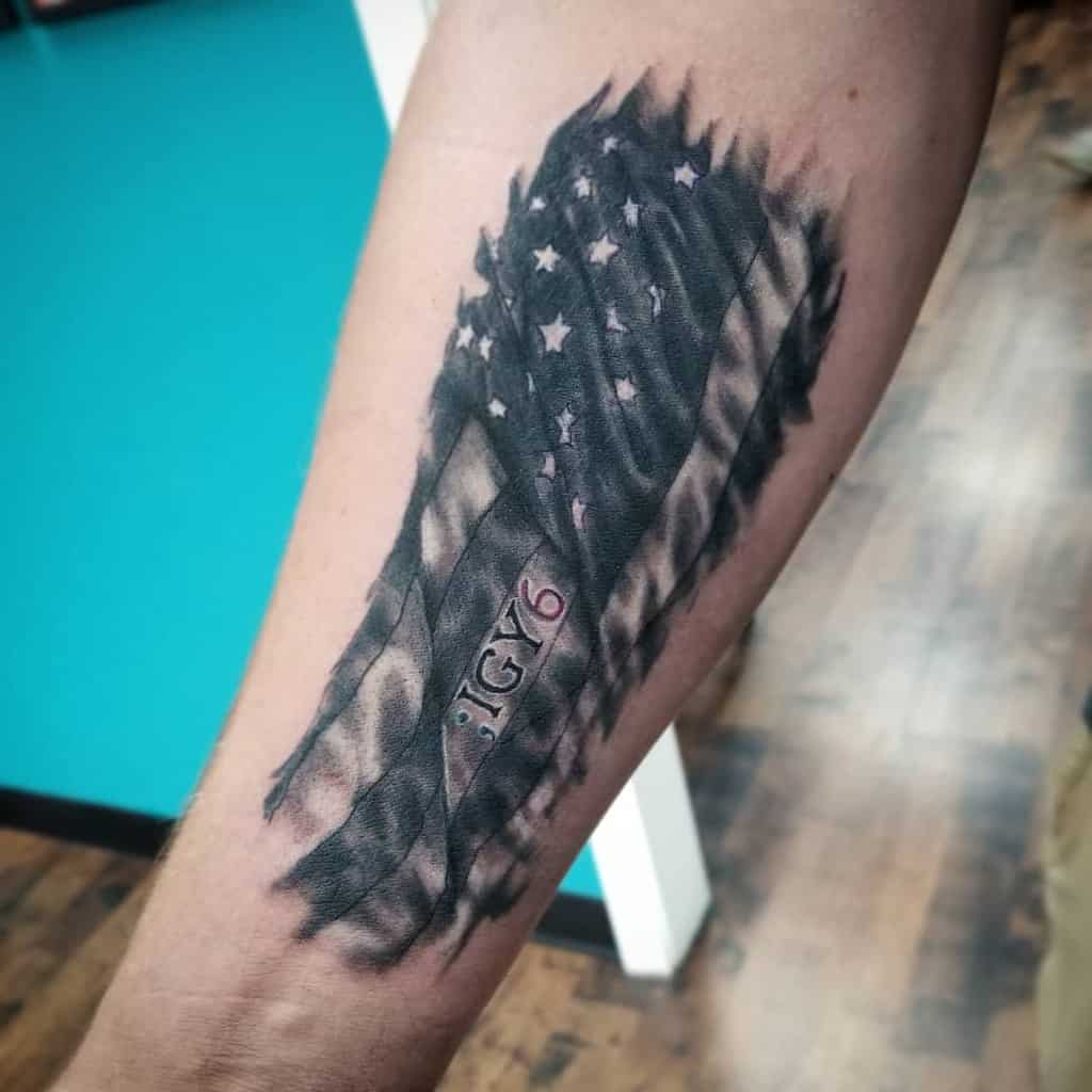 Tattoo of a tattered American flag on an arm with "IGY6" written below it