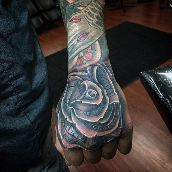A detailed black and gray tattoo of a rose on the hand, incorporating money elements, with deep shading and a realistic appearance