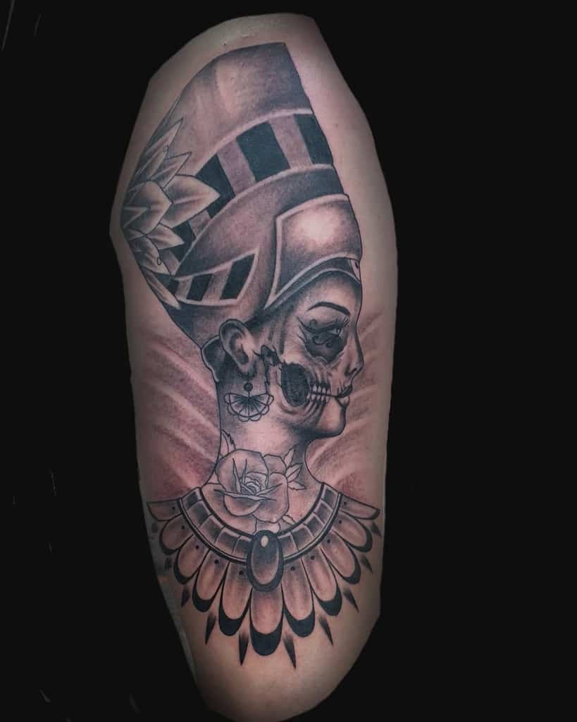 Tattoo of a woman with Nefertiti's floral headdress and skull face design on arm