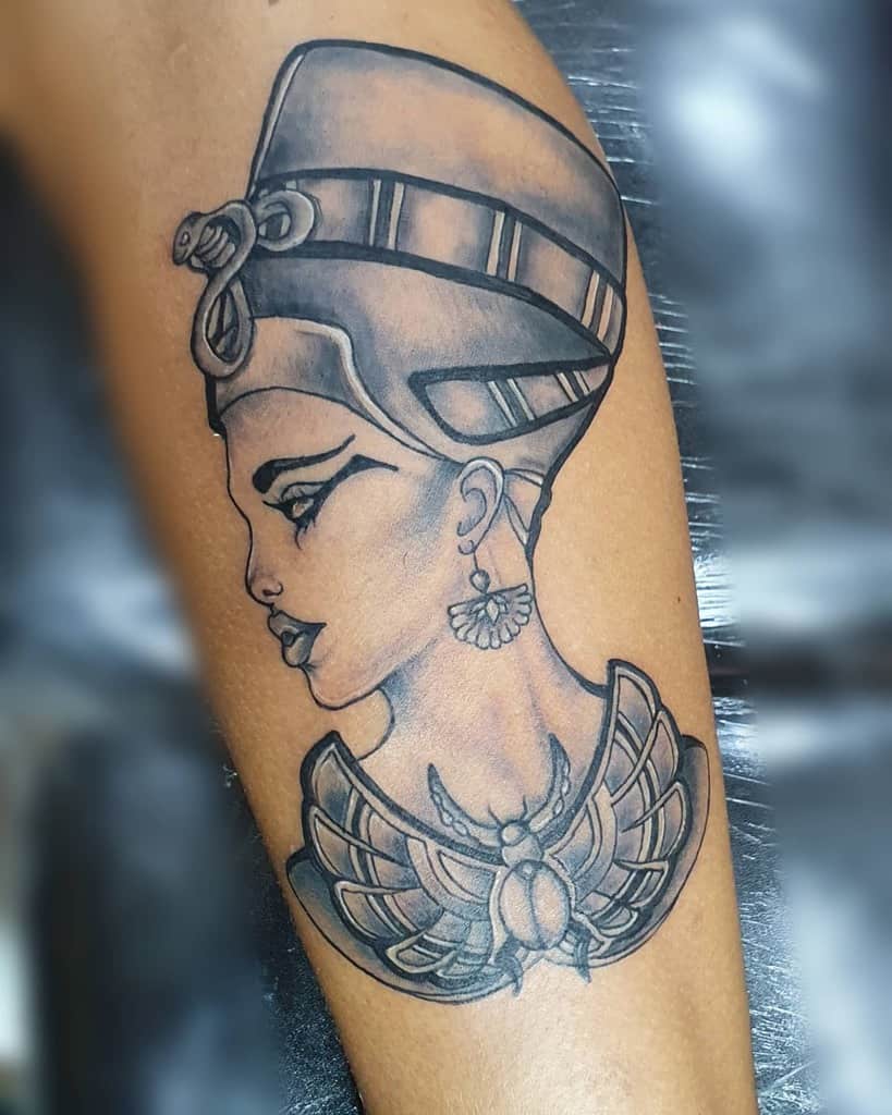 Tattoo of Nefertiti with a headpiece and earrings, and a winged scarab on the arm