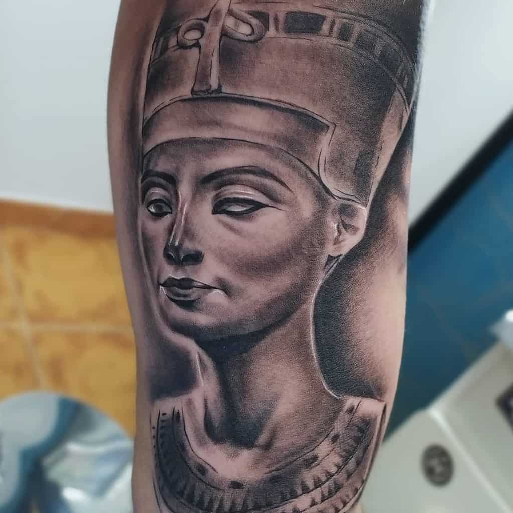 Tattoo of Nefertiti on an arm, showcasing a detailed headdress and collar