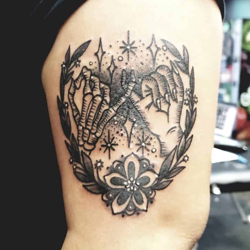 Tattoo of two hands making a pinky promise, surrounded by stars, leaves, and a flower